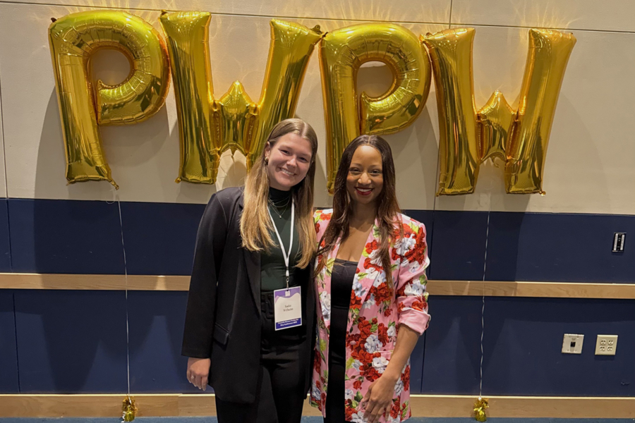 Two young women stand in front of large gold balloons that show the letters P W P W.